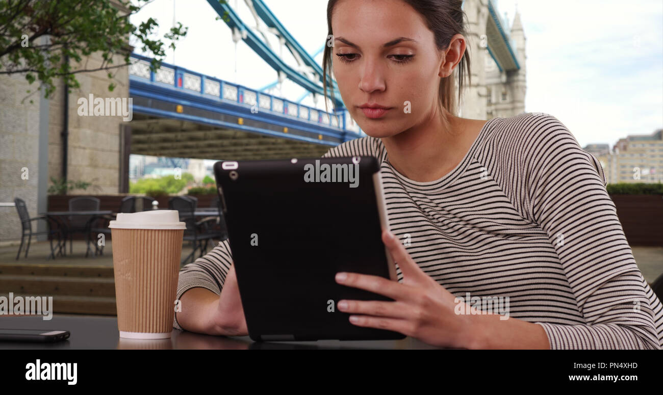Millennial woman sitting at cafe table with tablet in London by Tower Bridge Stock Photo