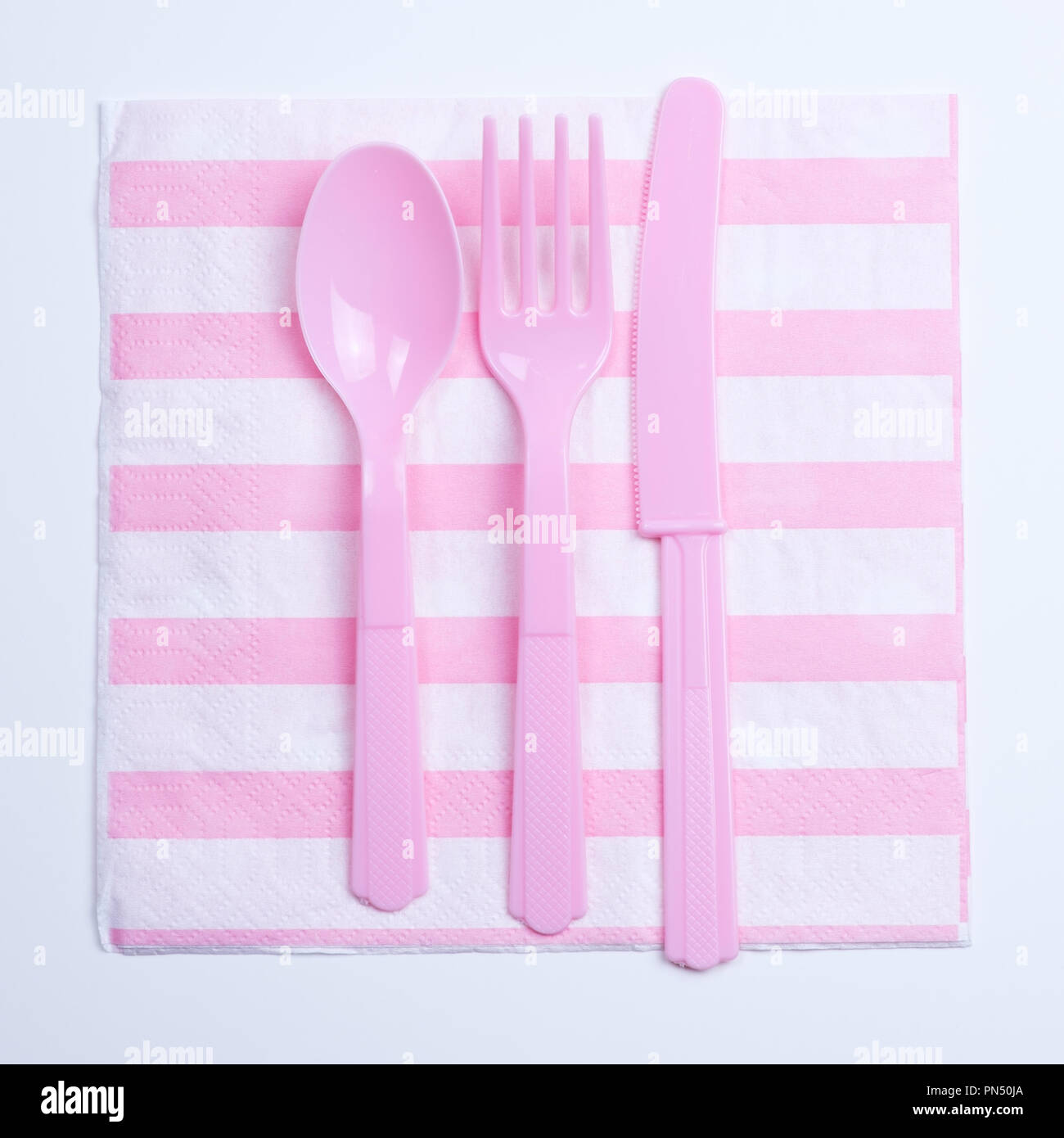 Pink color plastic fork, spoon and knife on napkin Stock Photo