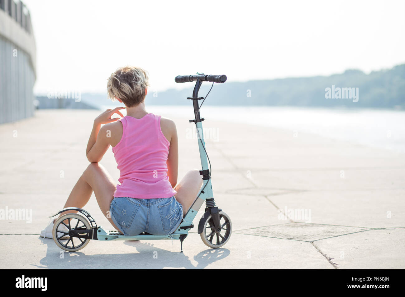 Positive blonde woman sitting at blue kick scooter Stock Photo