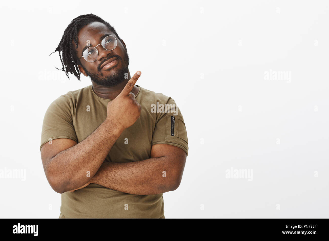 https://c8.alamy.com/comp/PN78EF/confident-joyful-dark-skinned-guy-in-trendy-glasses-holding-hand-crossed-on-chest-and-pointing-at-upper-right-corner-with-index-finger-gazing-at-direction-with-satisfied-dreamy-expression-PN78EF.jpg