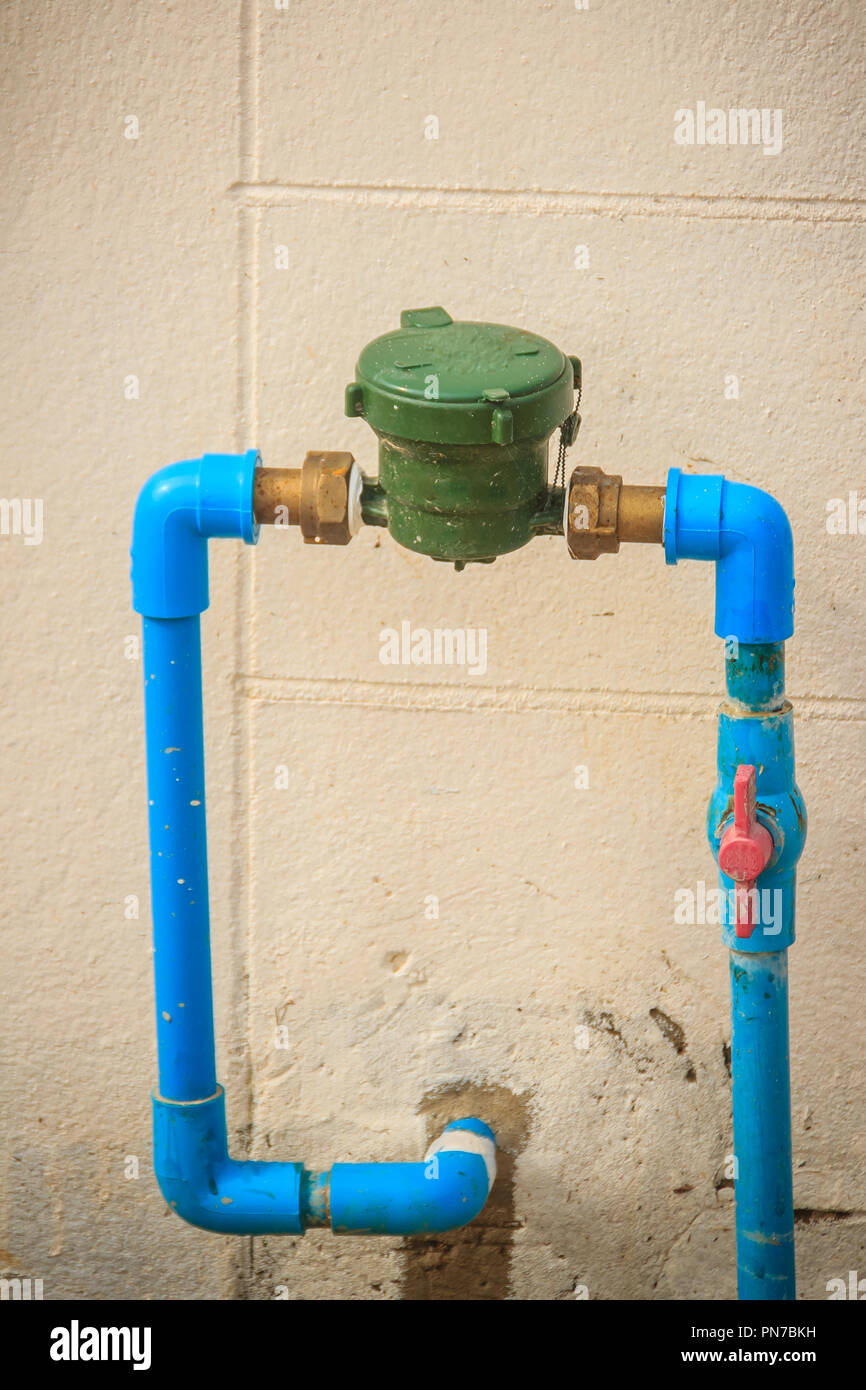 Vintage water meter installed with bronze joint, PVC elbow connector, blue  PVC pipe and red water valve on the grungy wall Stock Photo - Alamy