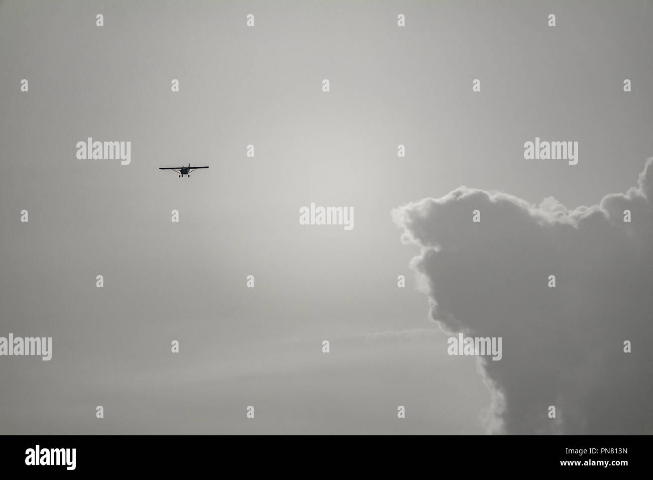 Small aircraft flying near huge clouds at dusk Stock Photo