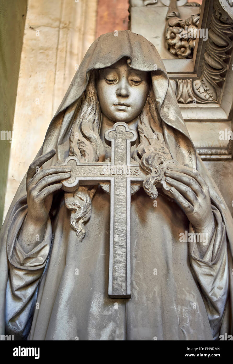 Pictures of a borgeoise realistic style stone sculpture of a girl holding a crucifix on the Poggi Family Tomb. The monumental tombs of the Staglieno M Stock Photo