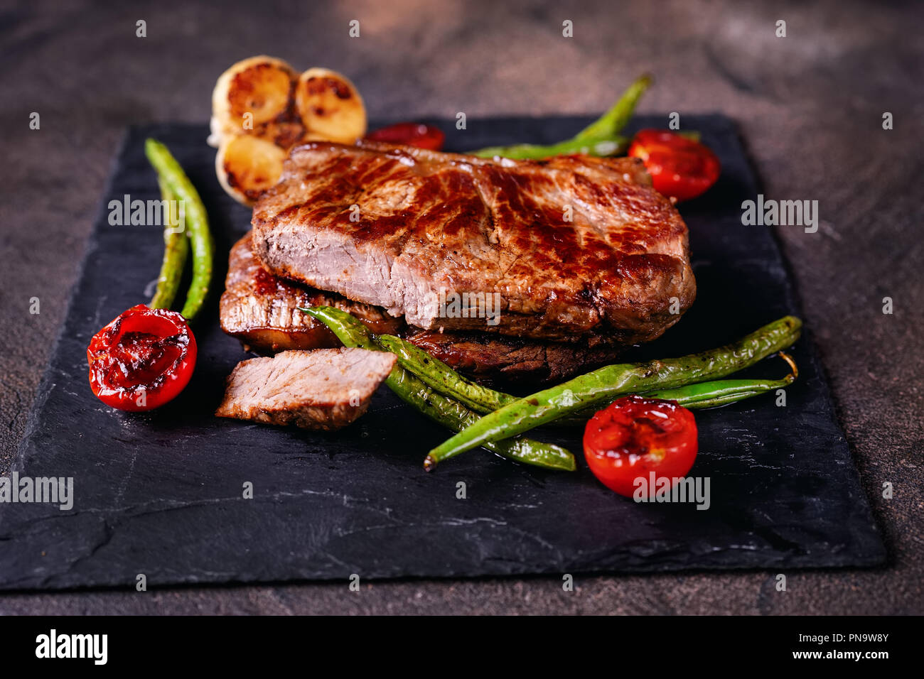 Prepared delicious beaf steaks with vegetables on slate plate Stock Photo