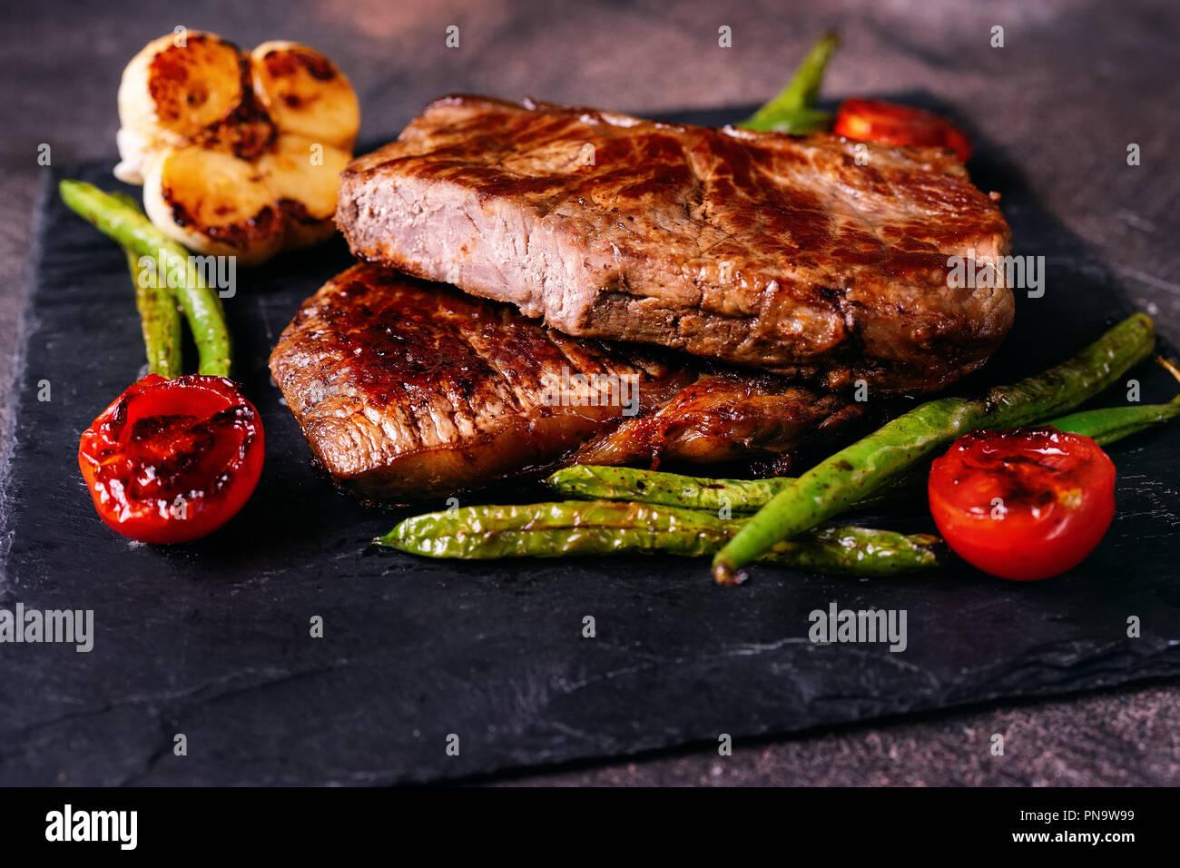 Prepared delicious beaf steaks with vegetables on slate plate. Close up. Stock Photo