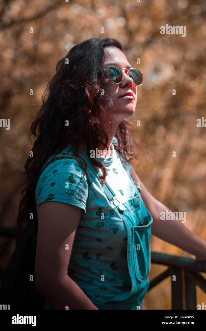 Portrait young brunette woman red hair with vintage sunglasses isolated in autumn forest wearing a denim romper Stock Photo