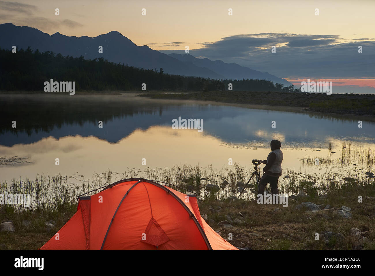Photographer taking a picture of beautiful lake and mountain near orange tent. Stock Photo