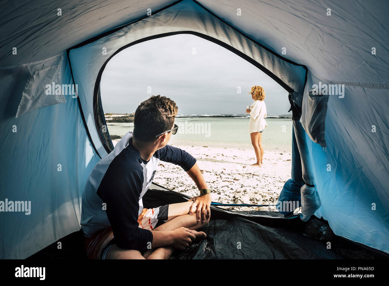 Alternative vacation enjoying total freedom with tent camped on the white sandy beach and blue ocean and sky. couple of caucasian people enjoying the  Stock Photo
