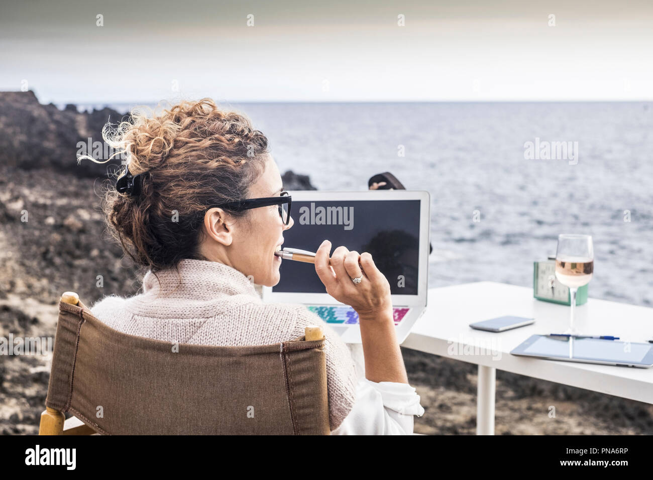 freedom and lifestyle for young woman at work in front of the ocean with no rooms and offices. laptop open and lady thinking at his career and his lif Stock Photo
