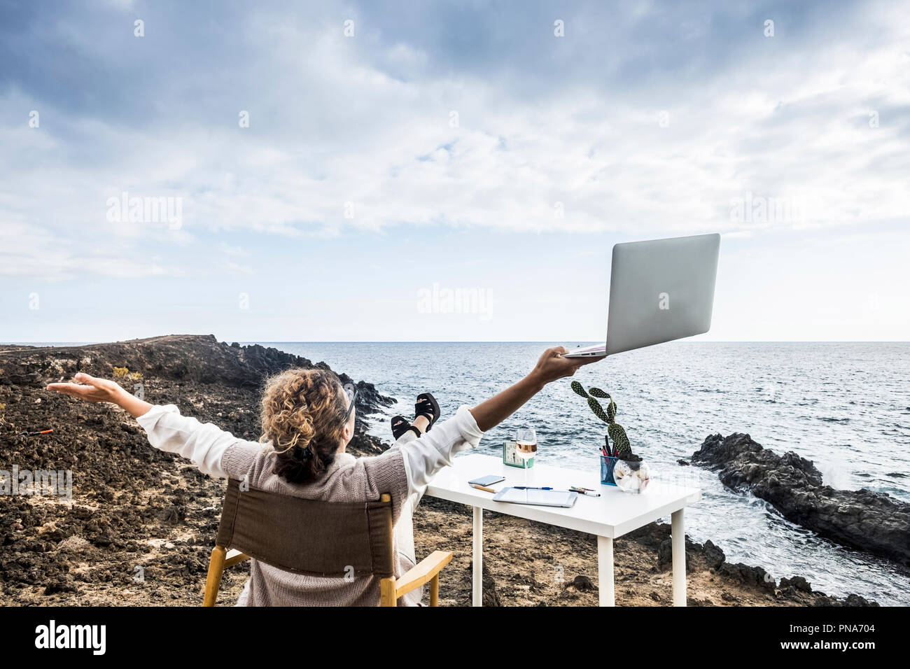 Middle age woman working in aleternative office in freedom in front of the ocean with no walls and buildings around. success and happiness concept for Stock Photo