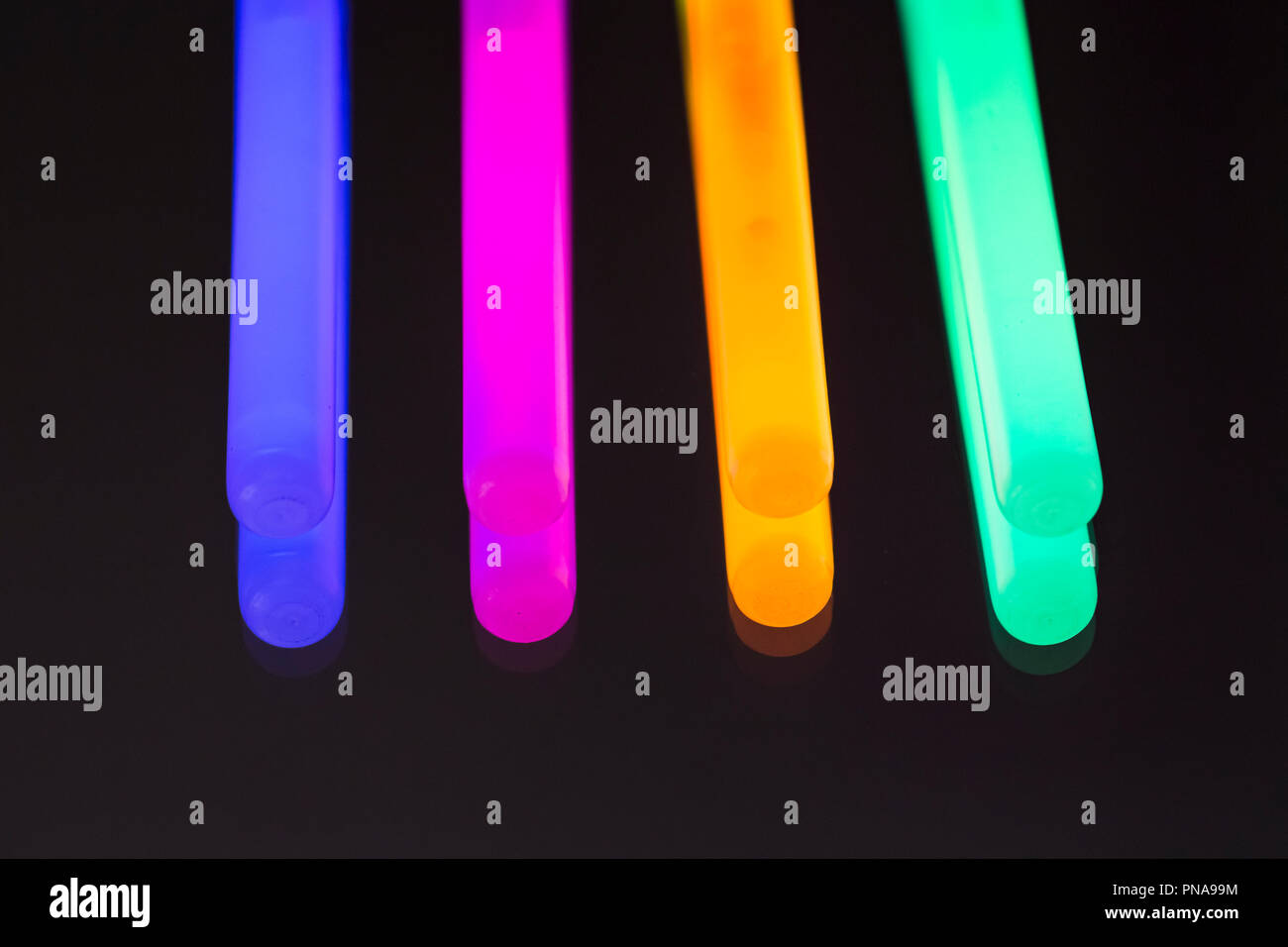 Colorful fluorescent light neon glow stick on mirror reflection black background. Blue pink