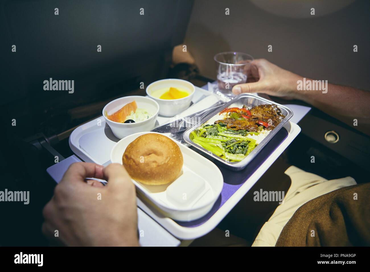 Traveling by airplane. Passenger enjoying dinner in economy class during long haul flight. Stock Photo