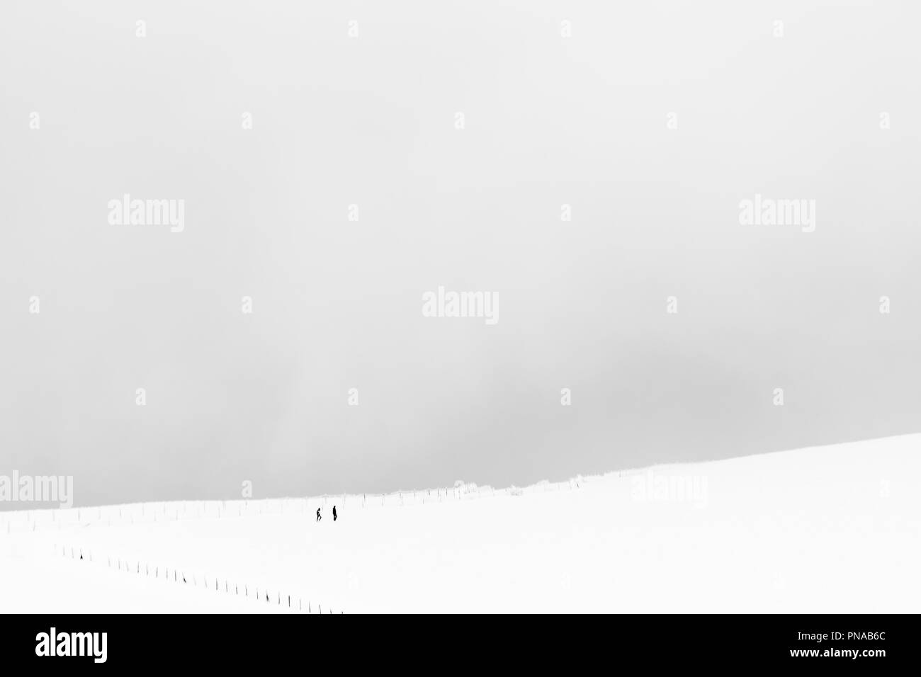 A very minimalistic view of two distant people over a mountain covered by snow, near a fence Stock Photo