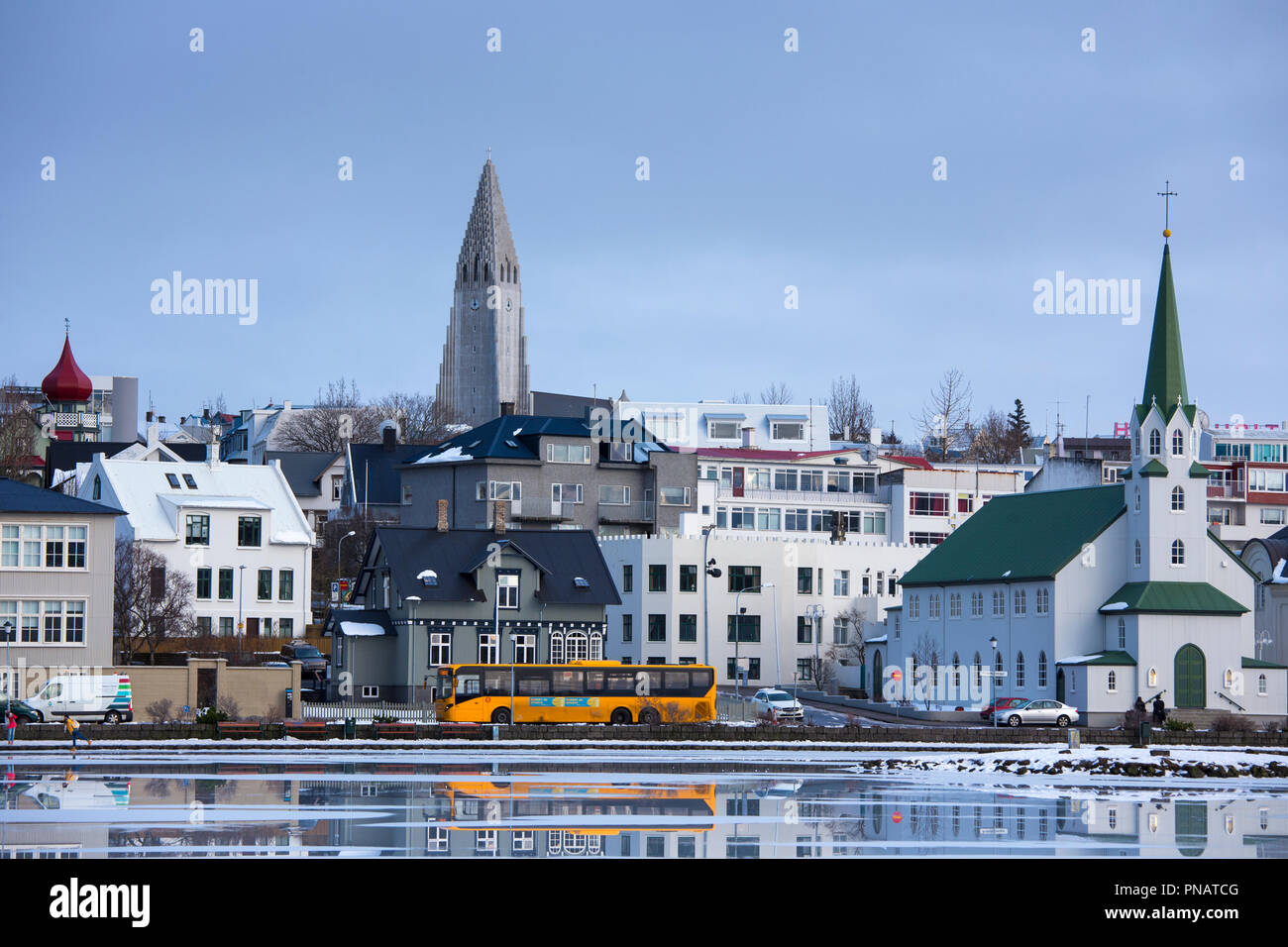Yellow bus - coach - in the capital city of Reykjavik and Lutheran church Hallgr’mskirkja Cathedral, Iceland Stock Photo