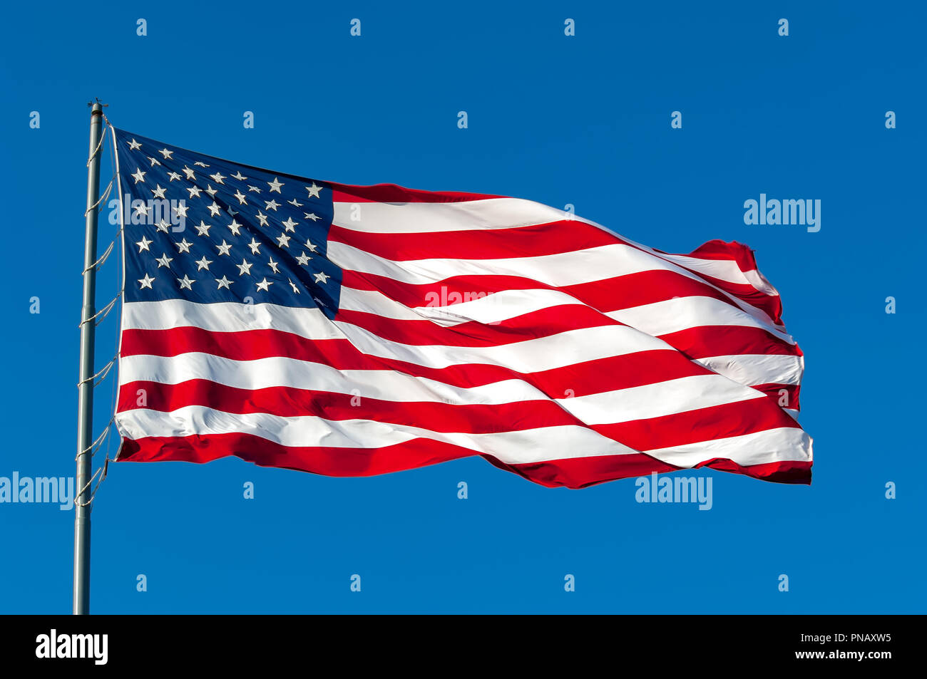 An American flag flying in the breeze against a cloudless bright blue sky. Stock Photo