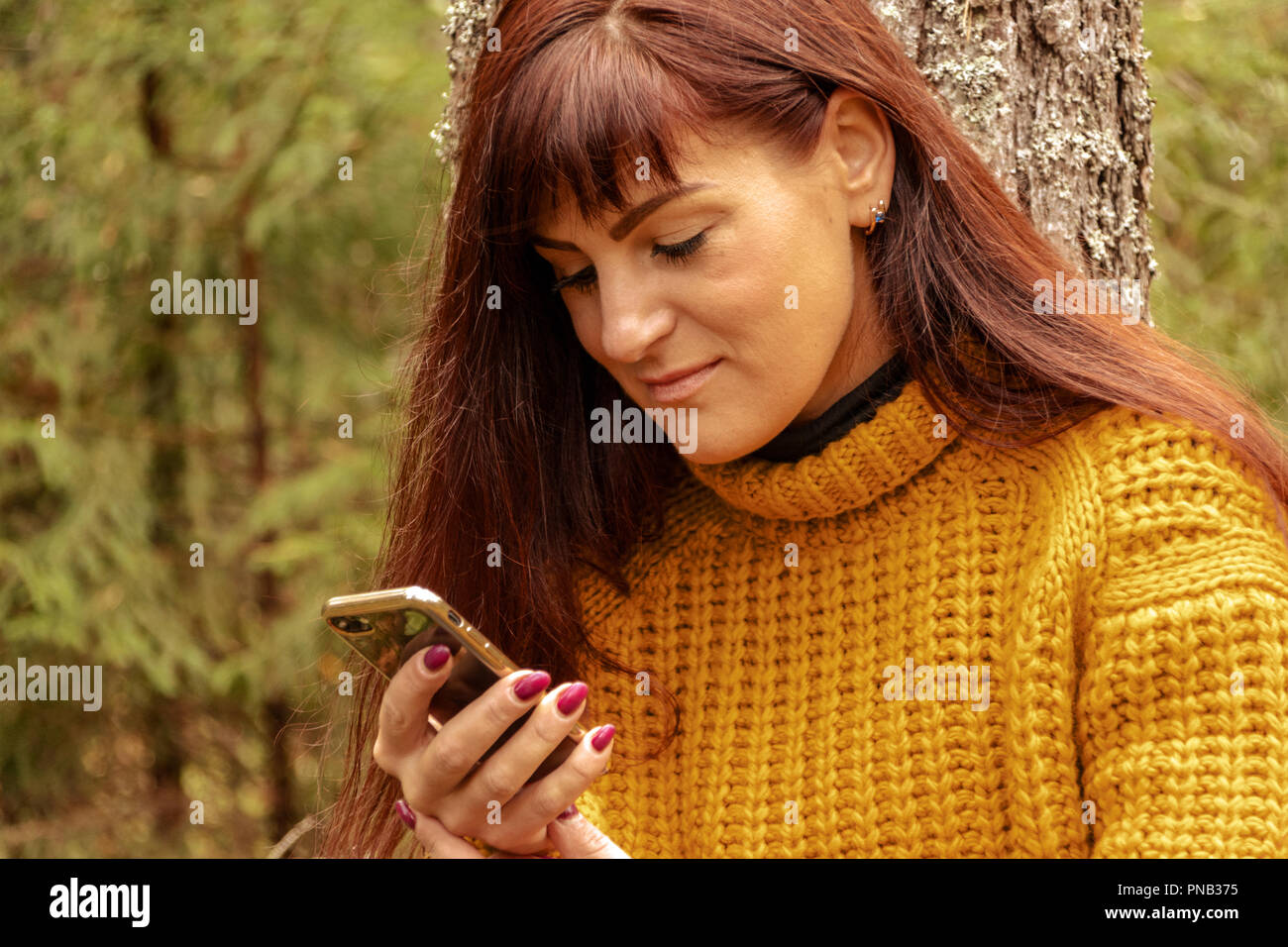 Girl looking at mobile phone in forest, toning Stock Photo