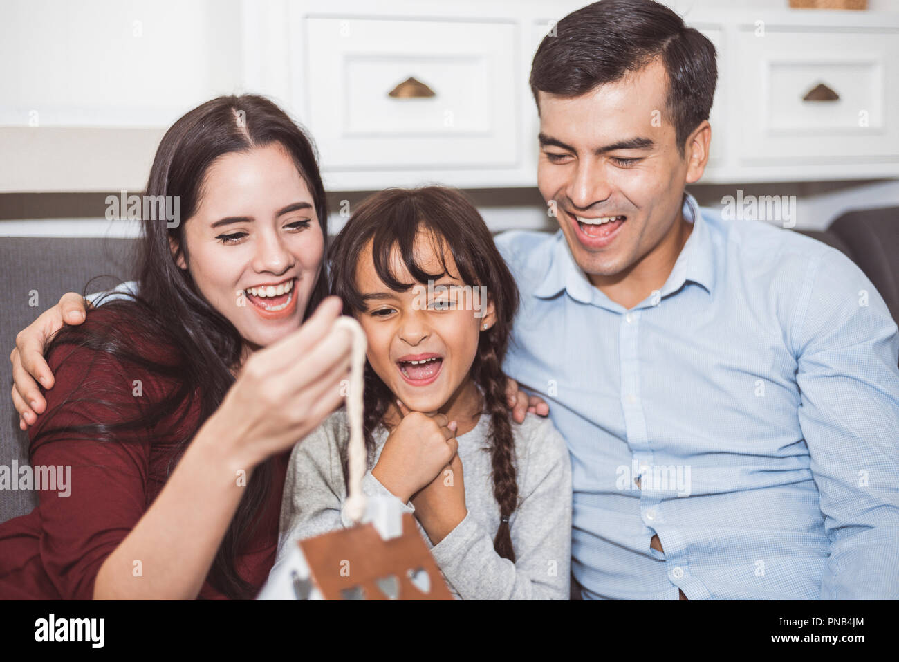 Father and mother surprise their daughter by gift or new toy. Parents and children are happy together in home on sofa in living room. Family and Happi Stock Photo