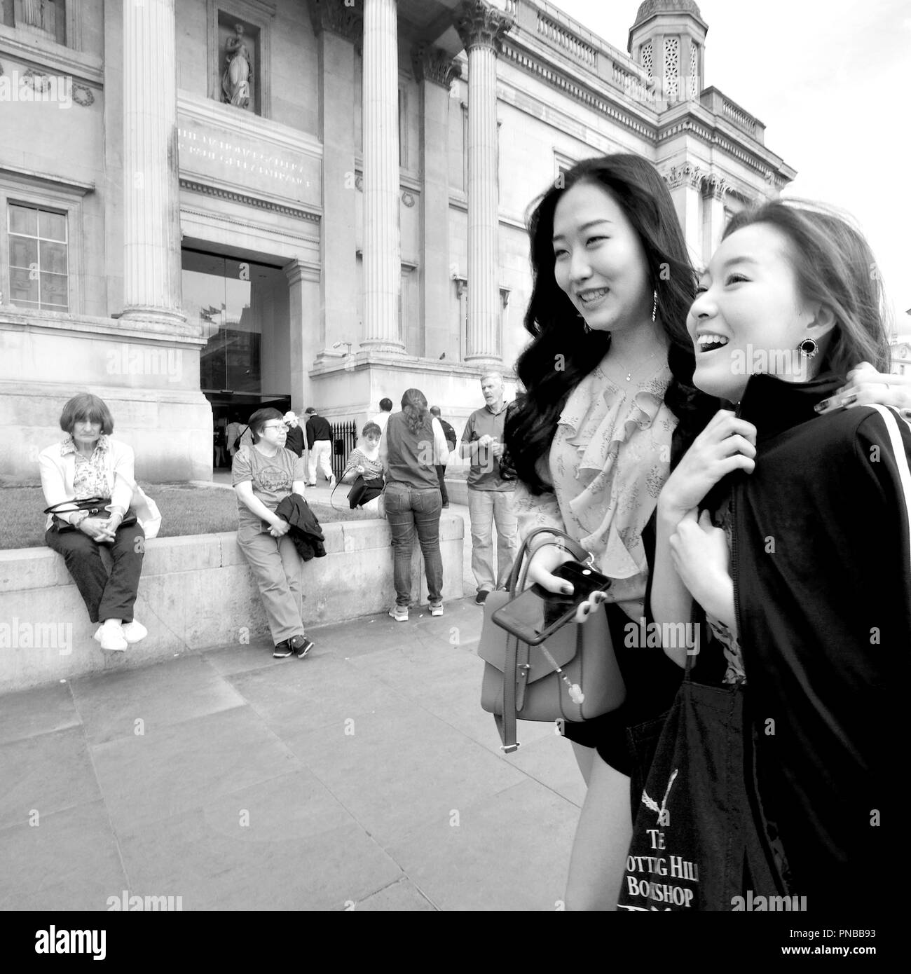 Two young Japanese women passing the National Gallery, Trafalgar Square, London, England, UK. St Martin in the Fields church behind Stock Photo