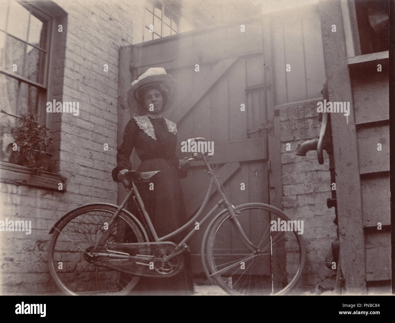 * Vintage Photograph of a Smartly Dressed Lady Stood in The Backyard of Her House With Her Bicycle Stock Photo