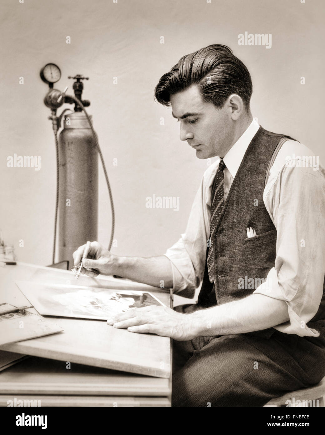 1930s MAN GRAPHIC ARTIST AIRBRUSHING A PHOTOGRAPH SEATED AT DESK BESIDE COMPRESSED AIR CLYINDER - a5561 HAR001 HARS CREATIVE AT OCCUPATIONS CYLINDER COMPRESSED AIR RETOUCHING SHIRTSLEEVES COMPRESSED CREATIVITY MID-ADULT MID-ADULT MAN BLACK AND WHITE CAUCASIAN ETHNICITY HAR001 OLD FASHIONED Stock Photo