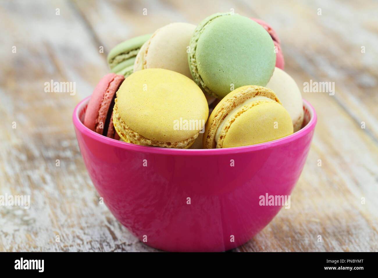 Colorful crunch macaroons in pink bowl on rustic wooden surface Stock Photo