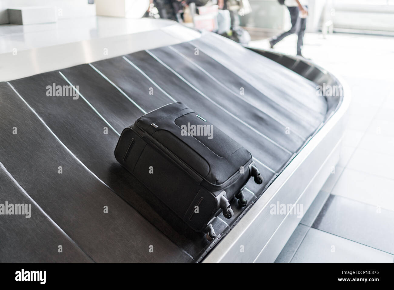 A smallsized black luggage bag is laying on a rotating black rubber