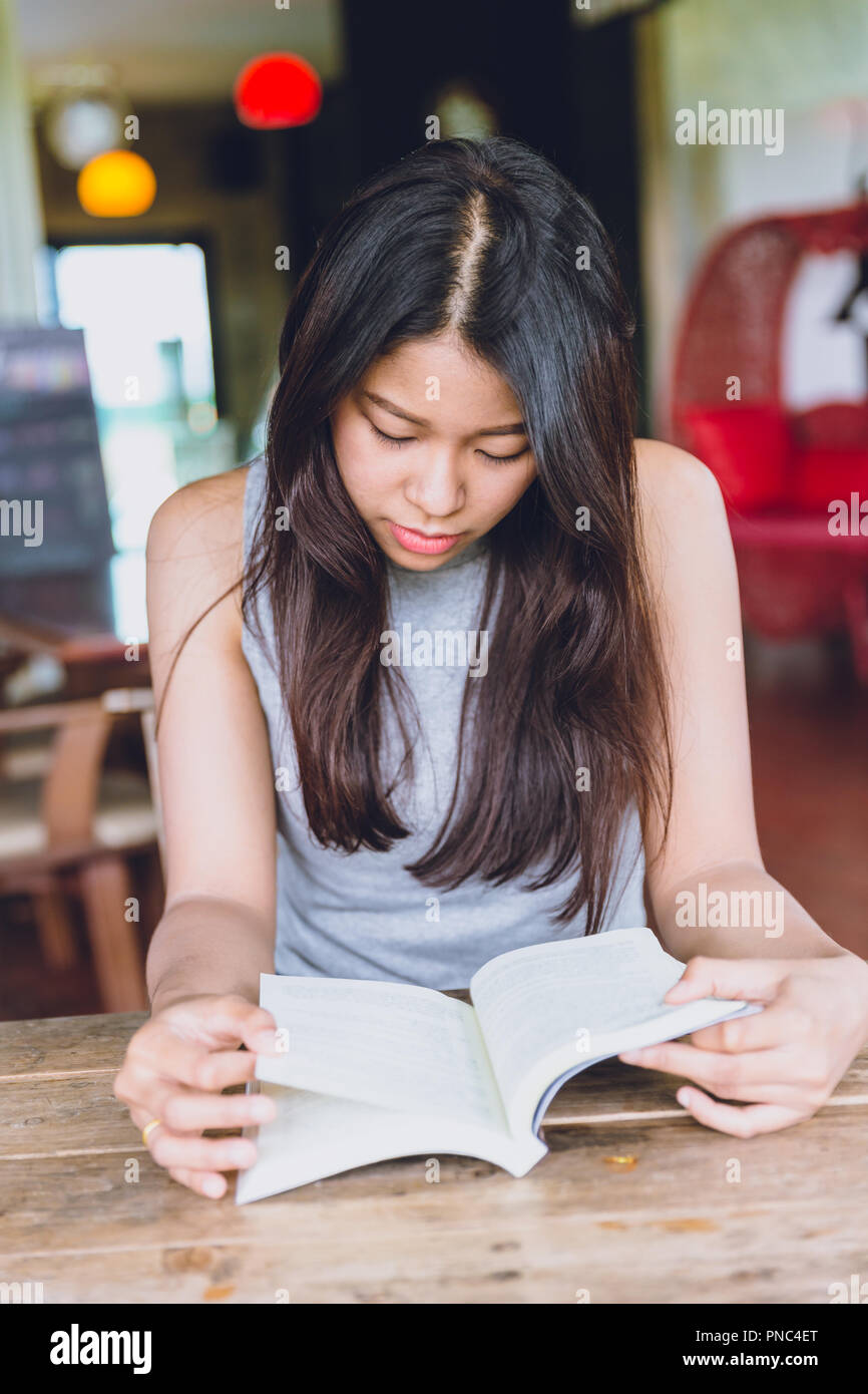 Enjoy relax times with reading book, Asian women Thai teen serious focus to read pocket book in coffee shop. Stock Photo