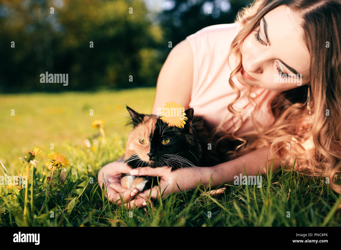Girl lying on grass with cat. Spring or summer warm weather concept. Bokeh background. Ginger kitten with two face color mask. Stock Photo