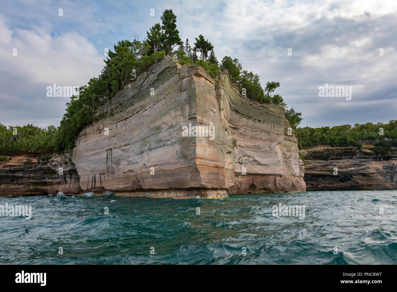A rocky point, covered with trees, displays the cliff face at Pictured Rocks National Lakeshore in Munising Michigan. The point is surrounded by the w Stock Photo
