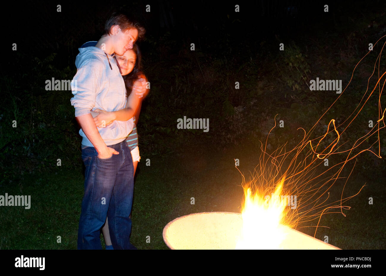 multi-ethnic couple looking at camp fire in fire pit Stock Photo