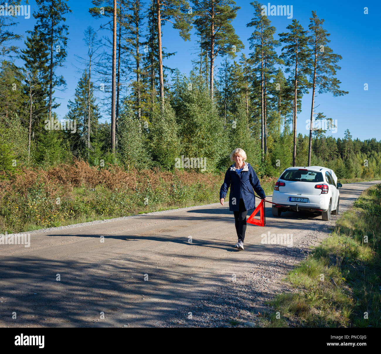 Woman with a broken car is putting a warnings triangel on the road Stock Photo