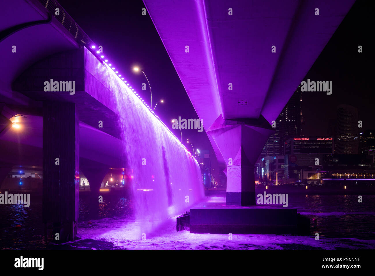 Illuminated waterfall from motorway bridge at night as part of the  Dubai Water Canal a waterway that connects into Dubai Creek and the sea. UAE, Stock Photo