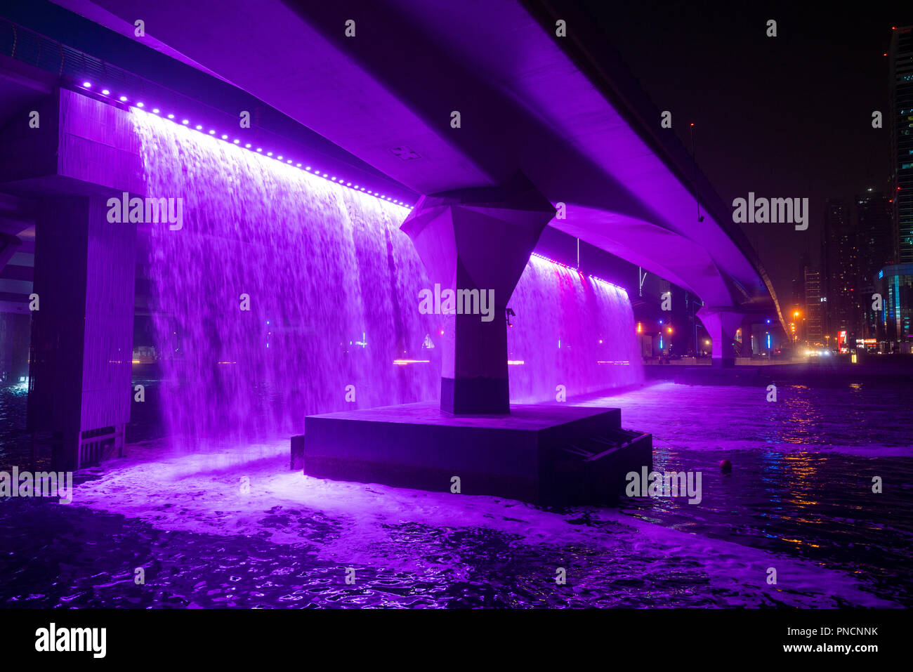 Illuminated waterfall from motorway bridge at night as part of the  Dubai Water Canal a waterway that connects into Dubai Creek and the sea. UAE, Unit Stock Photo