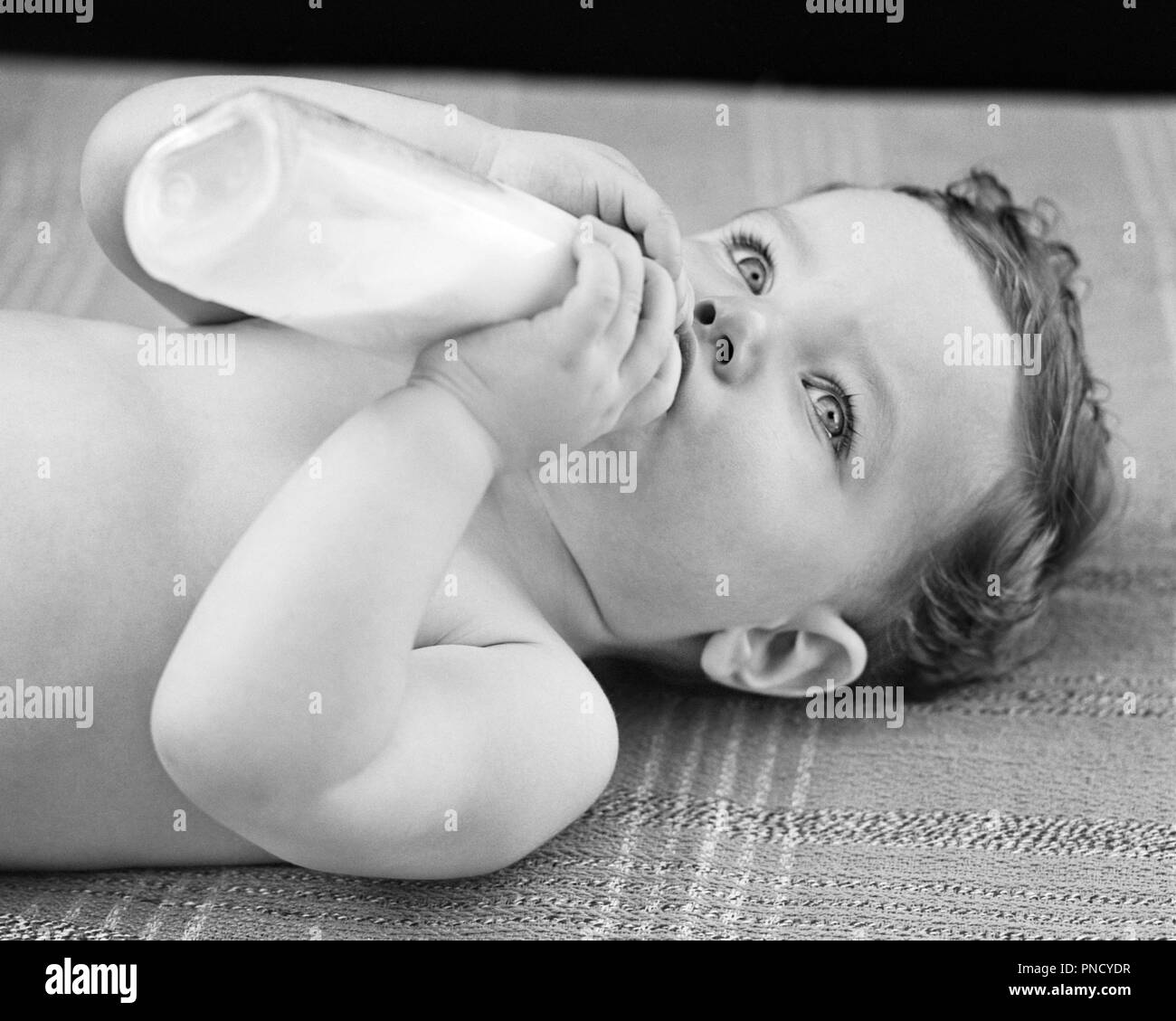 1940s Bright Eyed Baby Boy Lying On Back Feeding Himself From