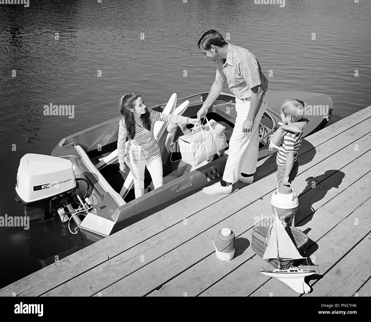 1970s FAMILY OF THREE FATHER MOTHER SON LOADING PICNIC COOLERS TOYS AND WATER SKIS INTO OUTBOARD MOTOR BOAT DOCKSIDE - b24696 HAR001 HARS RIVER NOSTALGIA OLD FASHION 1 JUVENILE BALANCE SAFETY TEAMWORK VACATION SONS FAMILIES JOY LIFESTYLE FEMALES MARRIED RURAL SPOUSE HUSBANDS HOME LIFE COPY SPACE FULL-LENGTH LADIES PERSONS SCENIC MALES RISK CONFIDENCE TRANSPORTATION FATHERS B&W LOADING TIME OFF HAPPINESS HIGH ANGLE ADVENTURE LEISURE AND GETAWAY DADS EXCITEMENT EXTERIOR KNOWLEDGE RECREATION MOTOR BOAT INTO OF HOLIDAYS CONNECTION ESCAPE STYLISH CARRIERS COOLERS DOCKSIDE COOPERATION JUVENILES Stock Photo