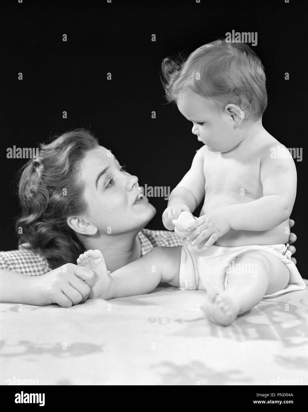 1940s ALERT BABY DAUGHTER SITTING UPRIGHT LOOKING FACE TO FACE AT EXPRESSIVE MOTHER WHO IS PINCHING HER FOOT - b2521 HAR001 HARS JUVENILE FACIAL COMMUNICATION YOUNG ADULT TEAMWORK INFANT STRONG JOY LIFESTYLE FEMALES HOME LIFE FULL-LENGTH LADIES PHYSICAL FITNESS DAUGHTERS PERSONS CARING EXPRESSIONS B&W IS UPRIGHT HAPPINESS HEAD AND SHOULDERS AT LOVING FACE TO FACE WHO CONNECTION EYE TO EYE ALERT CURIOUS STYLISH PERSONAL ATTACHMENT AFFECTION EMOTION JUVENILES MOMS TOGETHERNESS YOUNG ADULT WOMAN BABY GIRL BLACK AND WHITE CAUCASIAN ETHNICITY EXPRESSIVE HAR001 INQUISITIVE OLD FASHIONED Stock Photo
