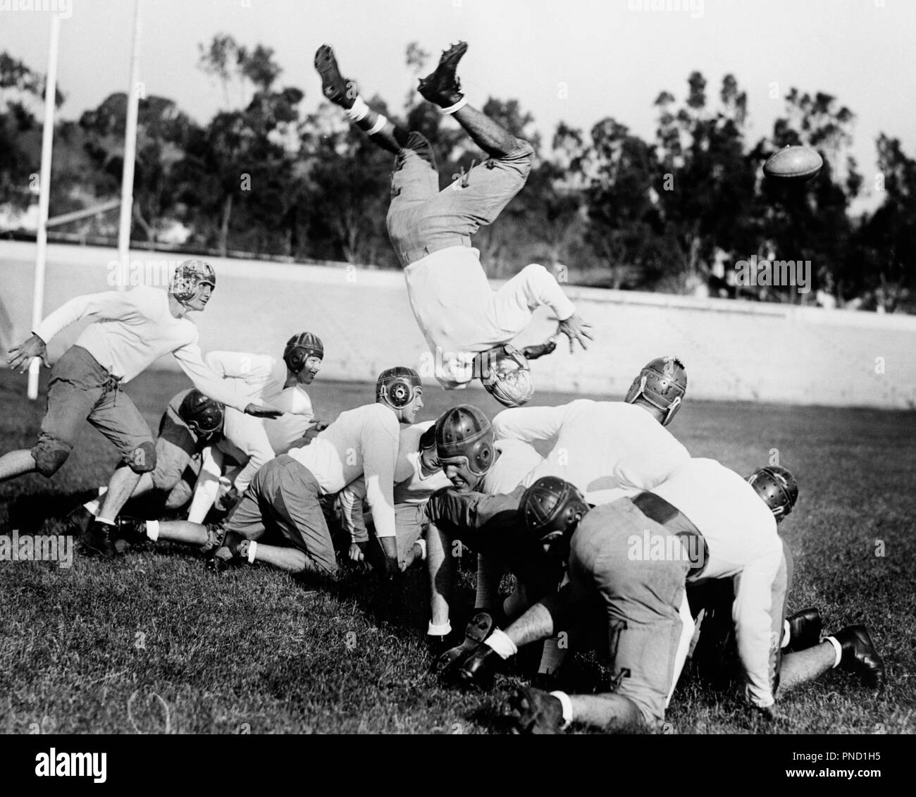 1930s 1940s LEATHER HELMET ERA FOOTBALL SCRIMMAGE LINE ONE PLAYER UPSIDE DOWN IN MIDAIR - gp0087 CAM001 HARS HORIZONTAL COPY SPACE PHYSICAL FITNESS PERSONS PRACTICE MALES ATHLETIC TACKLE AMERICANA B&W GOALS ACTIVITY PHYSICAL STRENGTH UNIVERSITIES EXCITEMENT QUARTERBACK RECREATION CAM001 UNIFORMS HIGHER EDUCATION ATHLETES FLEXIBILITY MIDAIR MUSCLES SCRIMMAGE COLLEGES HELMETS LEATHER HELMETS SACKED YOUNG ADULT MAN BLACK AND WHITE CAUCASIAN ETHNICITY ERA OLD FASHIONED UPSIDE DOWN Stock Photo