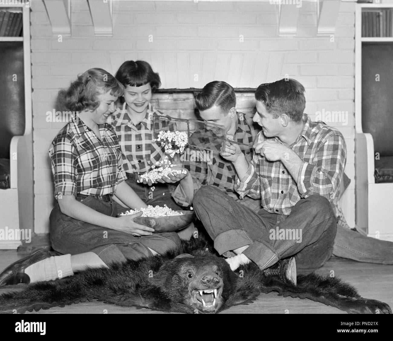 1950s GROUP TEENS POPPING POPCORN SMILE LAUGHING JOKING AROUND BEAR SKIN RUG FIREPLACE WEARING PLAID SHIRTS JEANS - j3343 LAN001 HARS TEAMWORK RUG PLEASED JOY LIFESTYLE CELEBRATION FEMALES HEALTHINESS HOME LIFE COPY SPACE FRIENDSHIP HALF-LENGTH PERSONS CLOTH MALES TEENAGE GIRL TEENAGE BOY PLAID DENIM SKIN POPCORN B&W HAPPINESS SHIRTS SMILES JOYFUL POPPING STYLISH TEENAGED BOBBY SOX BLUE JEANS JOKING JUVENILES TOGETHERNESS WIRE BASKET BLACK AND WHITE CAUCASIAN ETHNICITY OLD FASHIONED Stock Photo