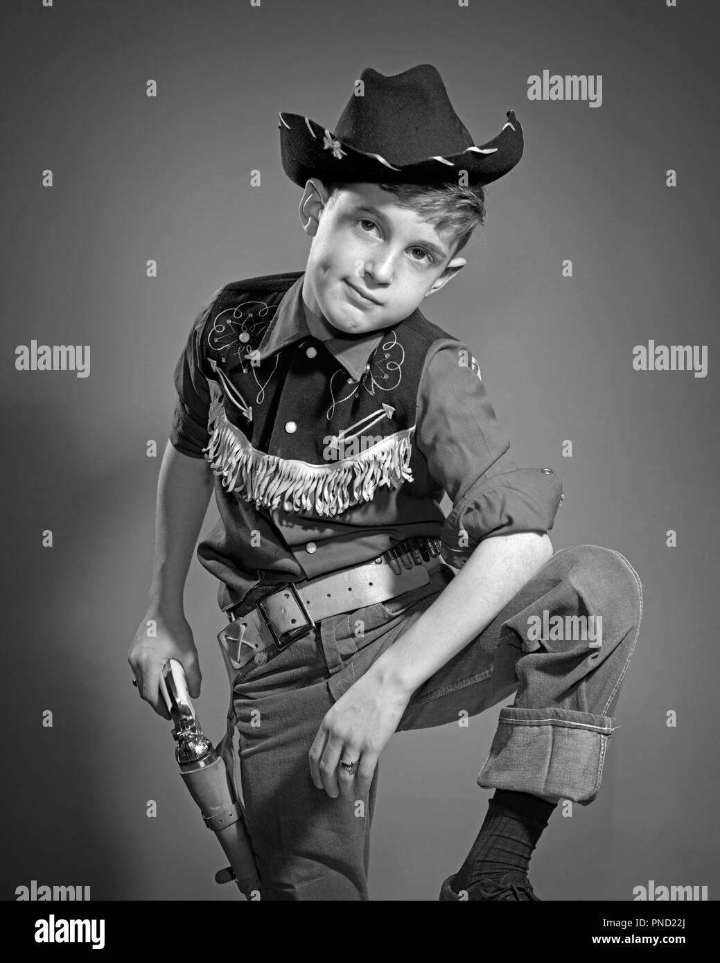 1950s BOY WEARING COWBOY HAT FRINGED WESTERN SHIRT LEATHER HOLSTER AND BELT  LOOKING AT CAMERA HAND ON CAP PISTOL SIX SHOOTER - j4224 DEB001 HARS EYE  CONTACT DREAMS ON CAP GUN IMAGINATION