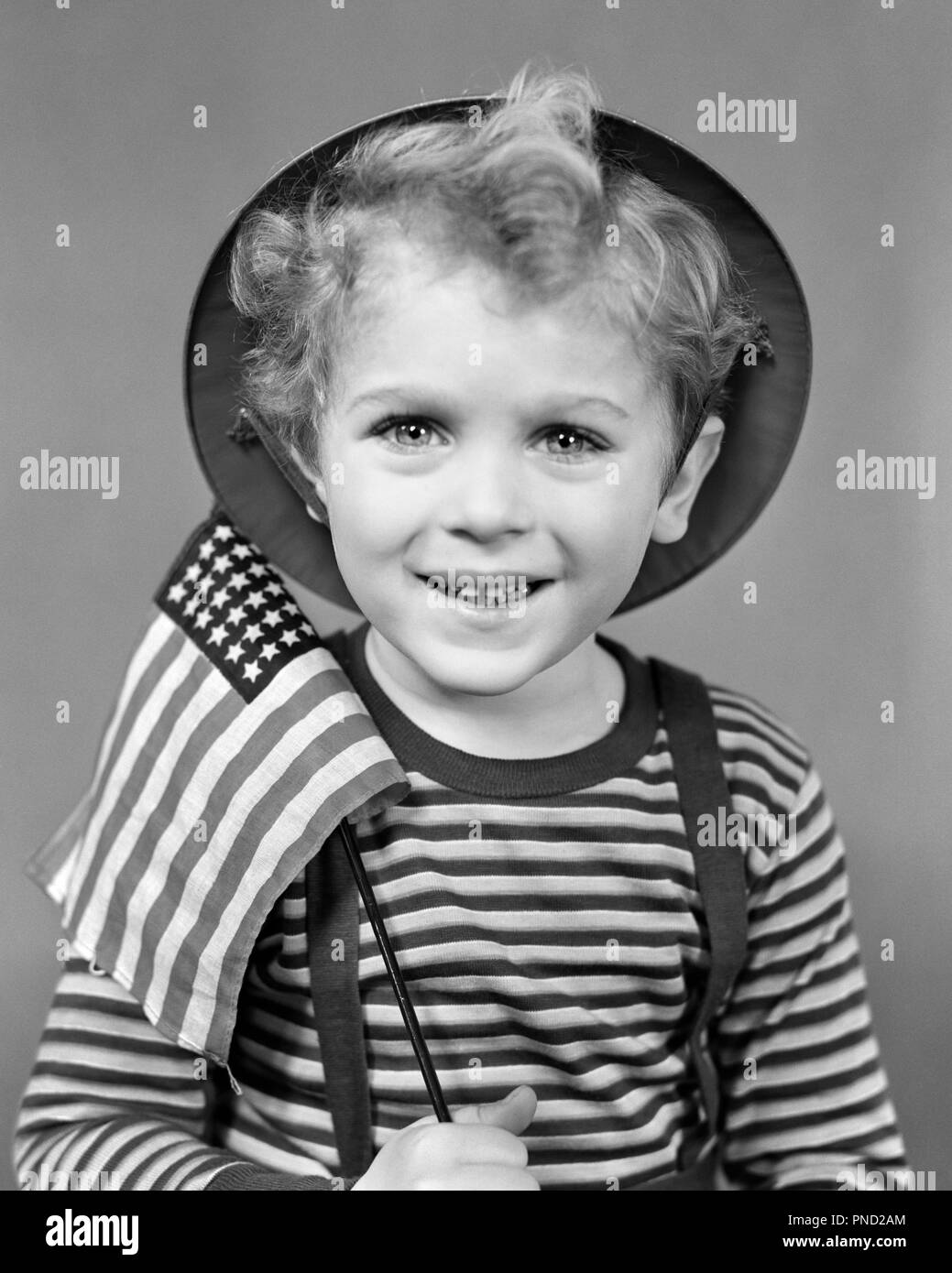 1940s SMILING CURLY HEADED BOY WEARING HAT &  STRIPED SHIRT AND HOLDING SMALL AMERICAN FLAG LOOKING AT CAMERA  - j8962 HAR001 HARS HOME LIFE UNITED STATES COPY SPACE HALF-LENGTH INSPIRATION UNITED STATES OF AMERICA MALES CONFIDENCE B&W EYE CONTACT FREEDOM HAPPINESS CHEERFUL AND WORLD WARS CURLY PRIDE WORLD WAR WORLD WAR TWO WORLD WAR II POLITICS SMILES JOYFUL PATRIOTIC STARS AND STRIPES WORLD WAR 2 48 STAR IDEAS JUVENILES RED WHITE AND BLUE STARS AND STRIPS BLACK AND WHITE CAUCASIAN ETHNICITY HAR001 HEADED OLD FASHIONED Stock Photo