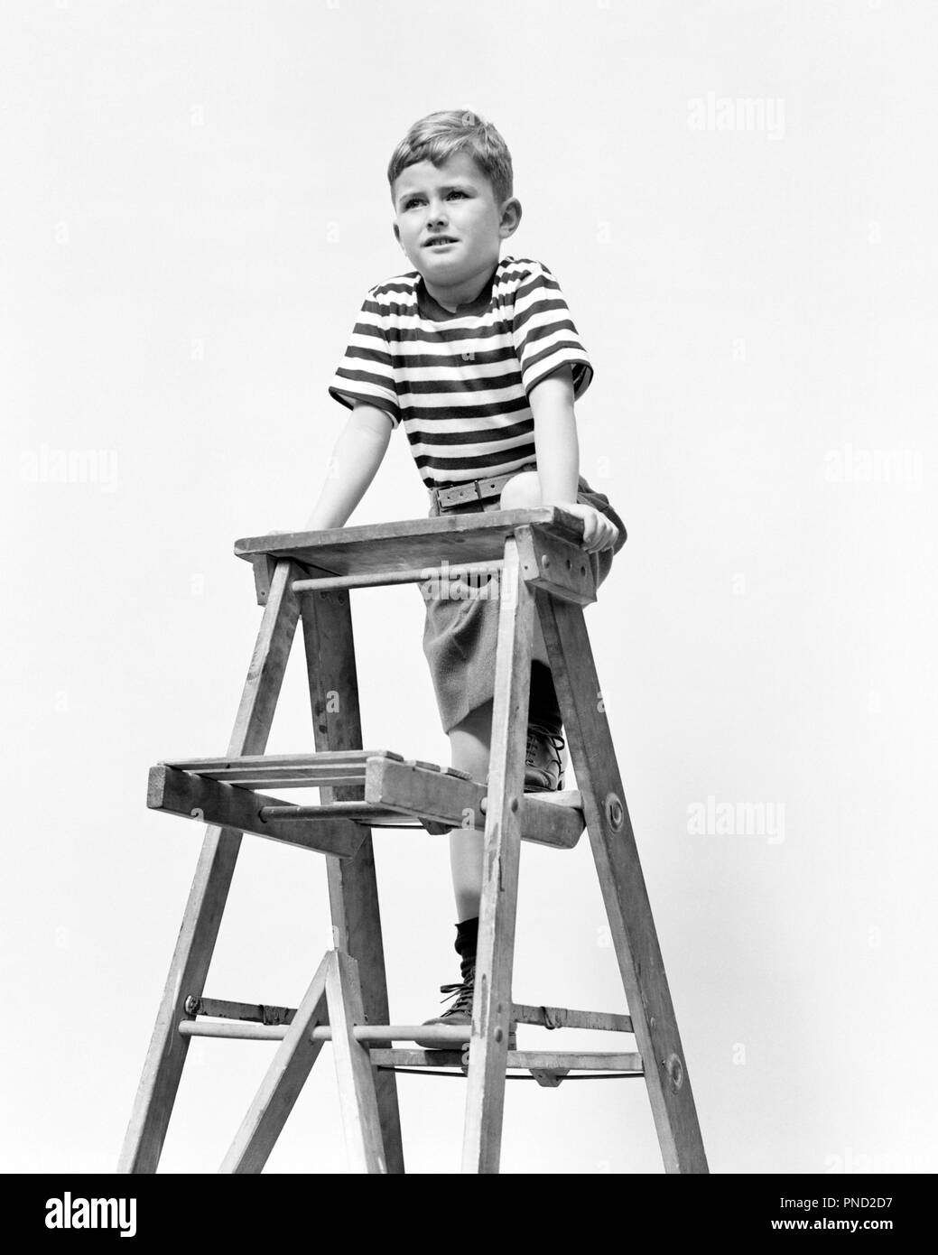 1940s BOY WEARING STRIPED T-SHIRT CLIMBING TALL STEP LADDER - j9766 HAR001 HARS CLIMB DANGEROUS STRENGTH COURAGE LOW ANGLE STEP LADDER T-SHIRT STEPLADDER AGGRESSIVE JUVENILES BLACK AND WHITE CAUCASIAN ETHNICITY HAR001 OLD FASHIONED Stock Photo
