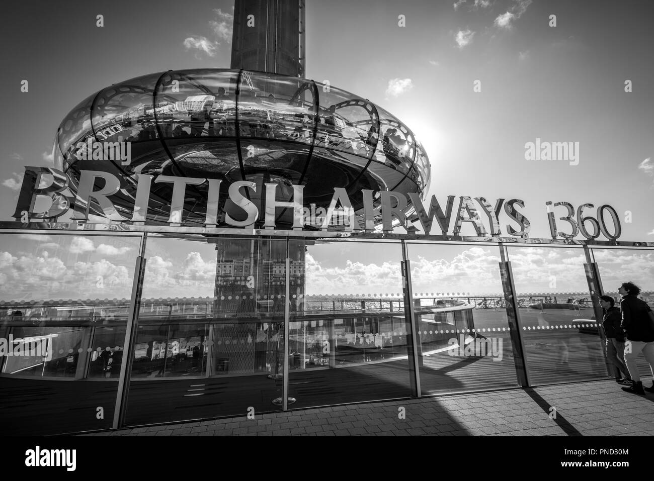 Tourists stand looking at the British Airways i360, an observation tower, on the seafront in Brighton, East Sussex, UK. Stock Photo