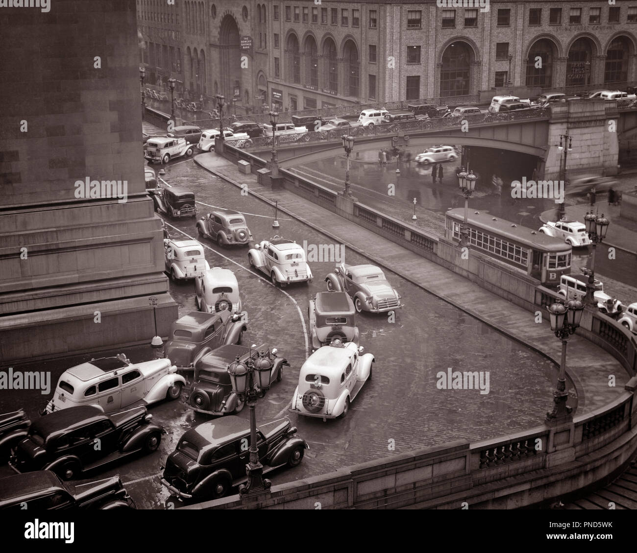 1930s RAINY DAY TRAFFIC JAM AROUND GRAND CENTRAL STATION AT PERSHING SQUARE AND 42ND STREET MIDTOWN MANHATTAN EASTSIDE NYC USA - q37701 CPC001 HARS AND AUTOS EXTERIOR PROGRESS DIRECTION AT NYC GRAND CENTRAL MOTION BLUR CONCEPTUAL NEW YORK AUTOMOBILES CITIES VEHICLES EASTSIDE NEW YORK CITY ROUNDING PERSHING SQUARE CONGESTION TAXIS 42ND STREET BLACK AND WHITE CABS OLD FASHIONED OVERPASS STREET CAR TROLLY Stock Photo