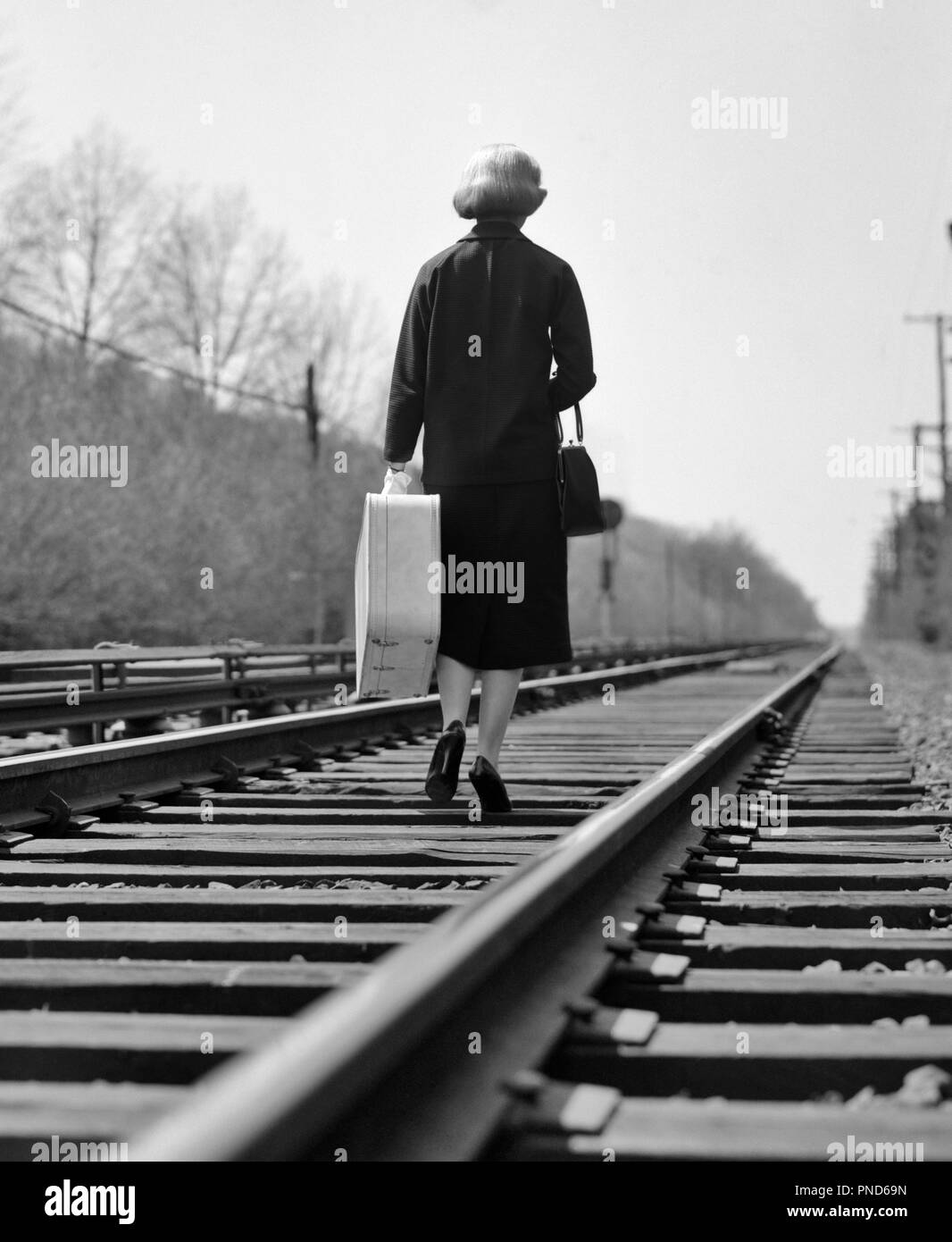 1950s 1960s BATTERED WOMAN ESCAPING BACK TO CAMERA WALKING DOWN RAILROAD TRACKS CARRYING SUITCASE LEAVING - s10060 DEB001 HARS FULL-LENGTH PERSONS GROWN-UP RISK SYMBOLS LEAVE B&W SADNESS TRACKS SINGLE FIGURE FREEDOM RUNAWAY VICTIM STRENGTH COURAGE CHOICE FED UP DIRECTION RIGHTS FINISHED HURT HURTING BACK TO CAMERA DONE SURVIVOR CONCEPTUAL ESCAPE SURVIVING DEB001 SYMBOLIC BATTERED GONE MID-ADULT MID-ADULT WOMAN MISERABLE PEOPLE ADULTS SYNDROME BLACK AND WHITE DESPERATE HAND BAG OLD FASHIONED REPRESENTATION Stock Photo