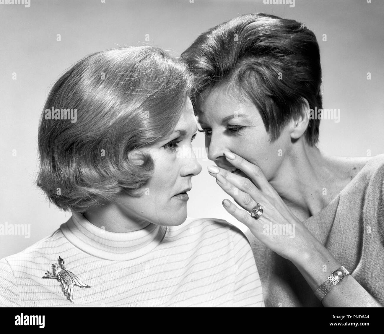 1960s 1970s TWO WOMEN SHARING SECRET AND GOSSIP ONE WHISPERING BEHIND HAND AND IN EAR OF OTHER  - s16701 HAR001 HARS FEMALES GOSSIP STUDIO SHOT HOME LIFE COMMUNICATING COPY SPACE FRIENDSHIP LADIES PERSONS CONFIDENCE SHARE GOSSIPING B&W TEMPTATION HEAD AND SHOULDERS STYLES NETWORKING EXCITEMENT KNOWLEDGE TELLING IN WHISPERS CONNECTION HAIRSTYLES RUMOR STYLISH ENTRE NOUS FASHIONS MID-ADULT MID-ADULT WOMAN SECRETS TOGETHERNESS BLACK AND WHITE CAUCASIAN ETHNICITY HAR001 OLD FASHIONED Stock Photo