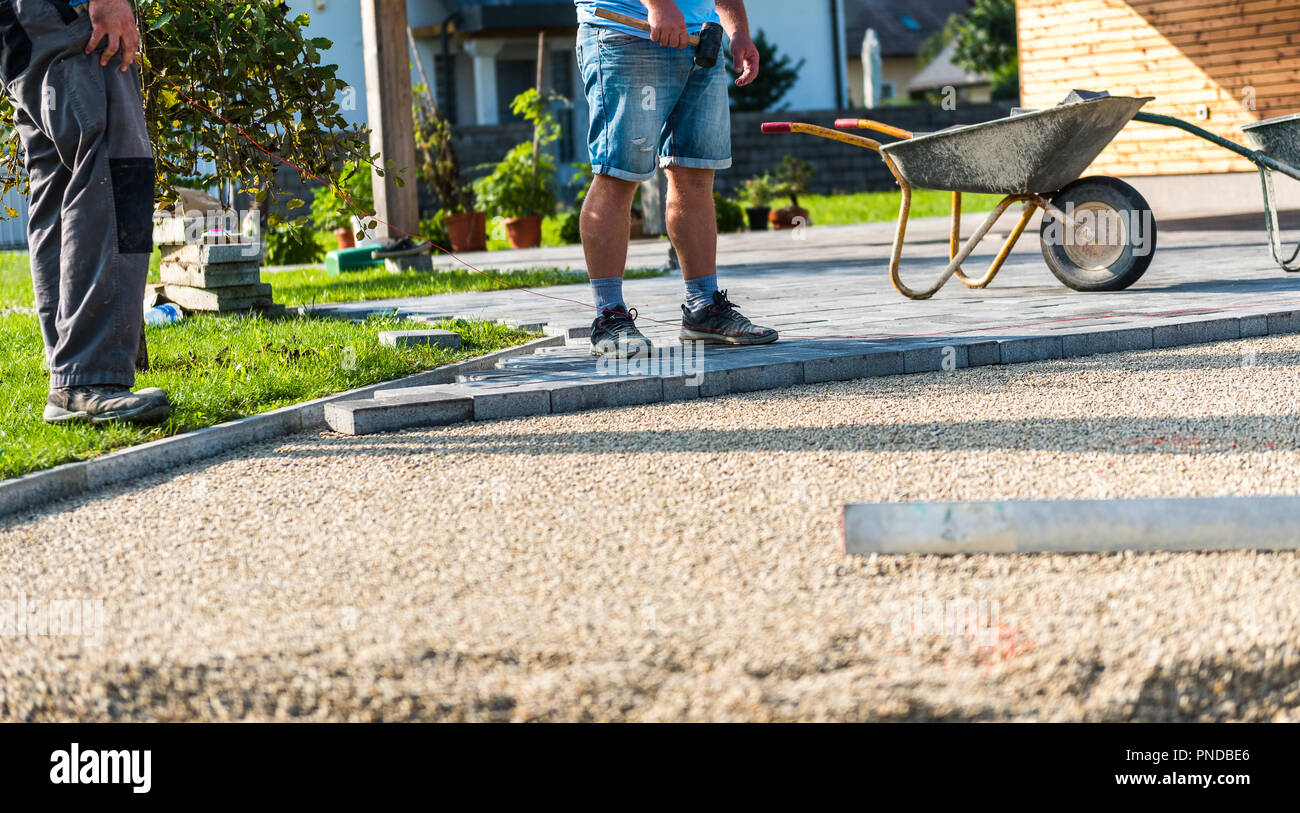 Laying gray concrete paving slabs in house courtyard driveway patio. Professional workers bricklayers are installing new tiles or slabs for driveway,  Stock Photo