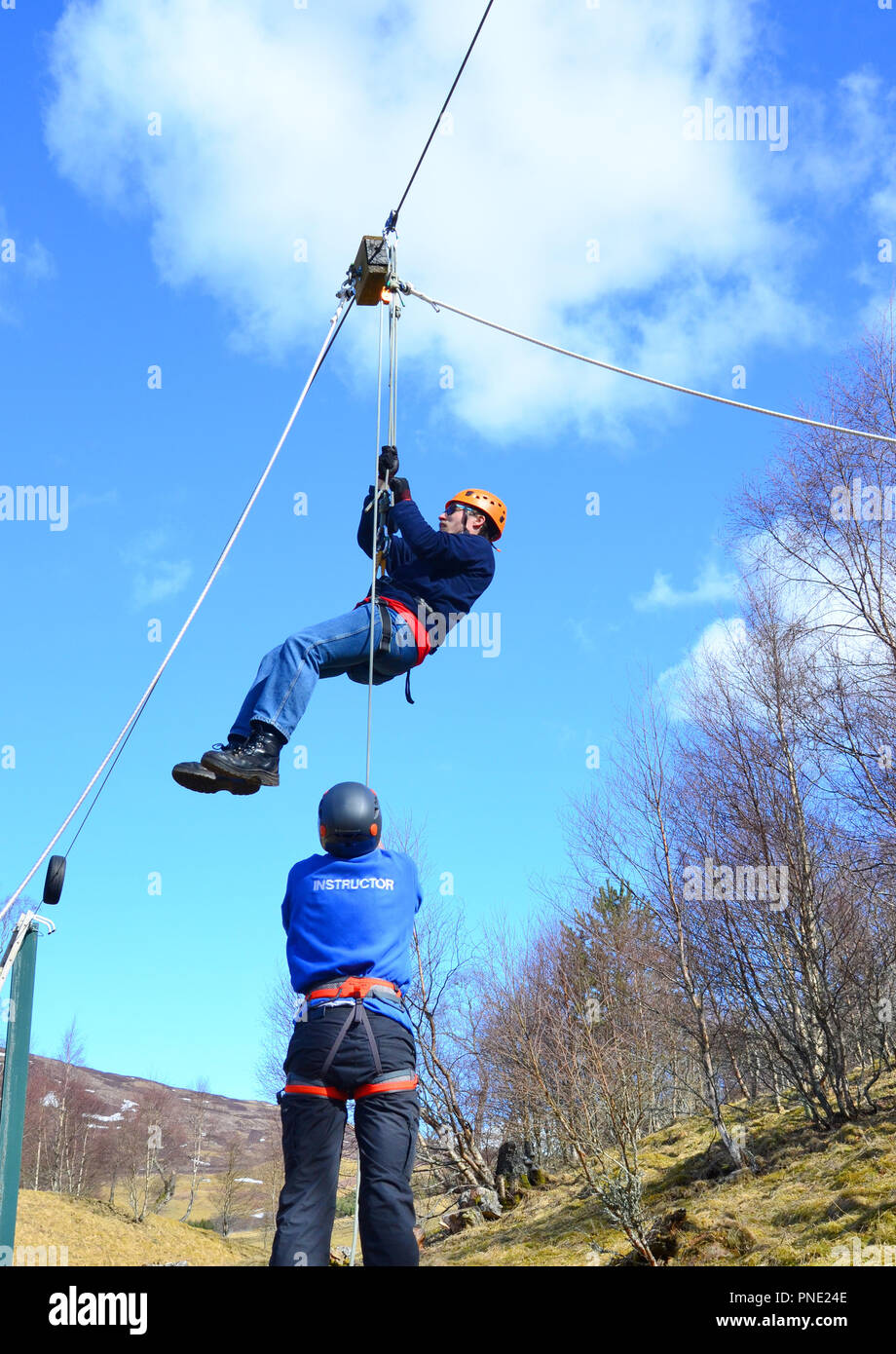 young man reaching the end of the zipwire and being aided down by the instructor Stock Photo