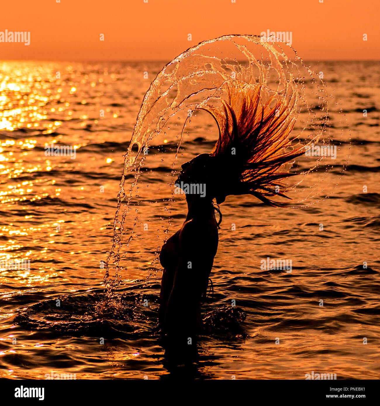 Teen Girl In A Dress With Long Hair At The Beach In Silhouette During Sunset Flipping Her Hair In The Water Stock Photo