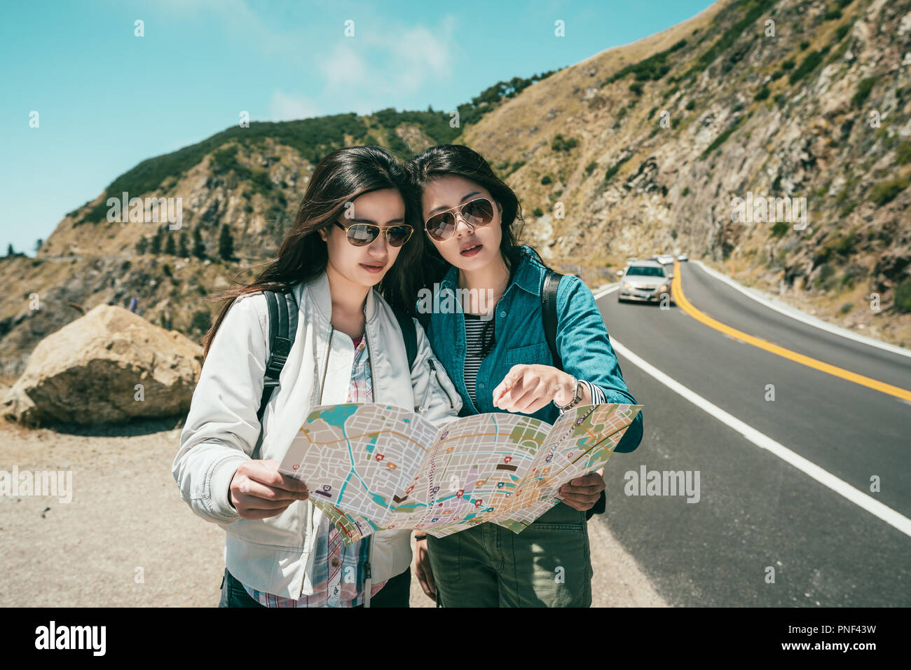 female travelers finding something on the guide map while standing on the road for a break time. Stock Photo