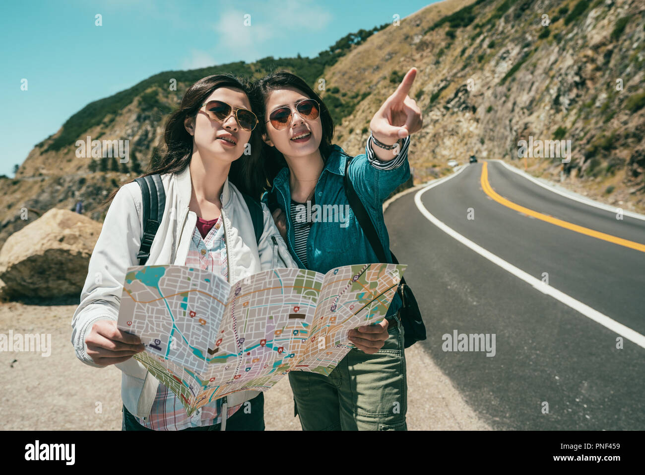 female tourists pointing to somewhere ahead excitingly and one of them holding a guide map. Stock Photo
